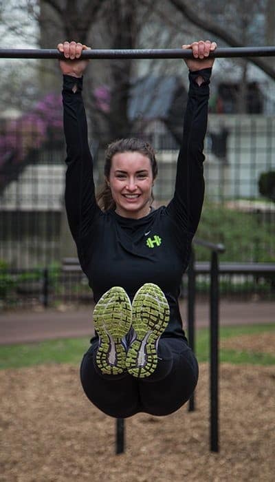 Smiling woman doing a hanging knee raise from a pull-up bar in a Chicago park