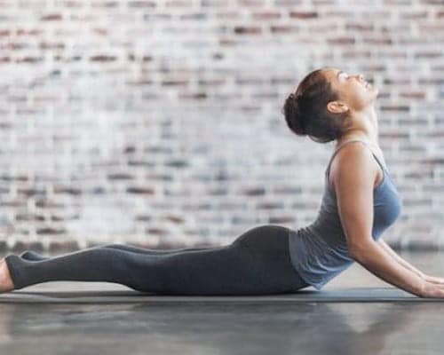 Woman holding a cobra stretch on a yoga mat in a brick-walled studio
